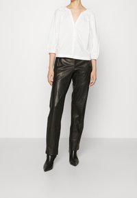 Weiße Baumwollbluse mit V-Ausschnitt und Puffärmeln, kombiniert mit schwarzen, eng zulaufenden Lederhosen und spitzen Stiefeletten.