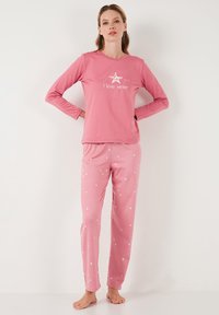 Camiseta de pijama de manga larga rosa con el texto blanco "Siempre amo el invierno", combinada con pantalones rosa con estampado de estrellas, ambos hechos de un tejido suave y elástico.