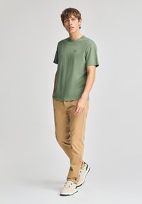 Grön t-shirt med kort ärm i kombination med beige chinos och beige sneakers. T-shirten har en diskret logotyp, slät textur och avslappnad passform.