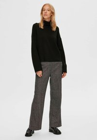 Pull à col roulé vert foncé au coupe ample et à ourlet côtelé, associé à un pantalon large en motif chevron gris et des bottines noires.