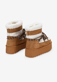 Botas de tobillo de ante marrón con puño de piel de oveja blanca, cordones texturizados y suela de goma gruesa con dibujo para mayor agarre.