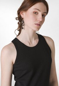 Svart ärmlös topp med rund halsringning, gjord av mjukt material. Modellen bär intrikata svarta örhängen med droppformade former.