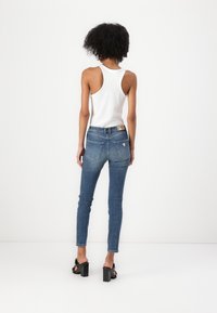 Jeans skinny blu con un lavaggio medio e leggeri sbiadimenti, abbinati a una canotta bianca a coste, con aperture sotto le braccia e una silhouette aderente.