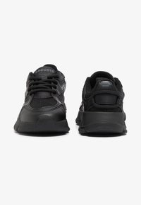Zapatillas deportivas negras con parte superior de malla y sintético, punta redonda, superficies texturizadas, parte delantera con cordones y suela acolchada. Logo de Lacoste en la lengüeta.