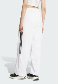 Biele voľné nohavice vyrobené z ľahkého materiálu s elastickým pásom. Majú tri vertikálne čierne pruhy na každej strane.