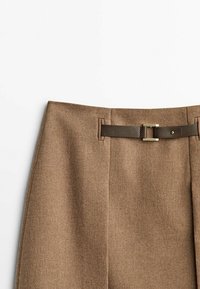 Pantalon en tissu brun texturé avec une coupe décontractée, doté d'une ceinture marron lisse et d'une boucle dorée. Comprend des plis avant ajustés.