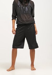 Top con capucha de malla negra con el logo "IVY PARK" y shorts de malla negra. Ambas prendas tienen un corte holgado y un diseño cómodo.