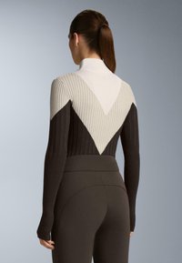 Dlhý rukáv rebrovaný top v krémovej, hnedej a tmavohnedej farbe s geometrickým V vzorom, s vysokým golierom a priliehavým strihom.