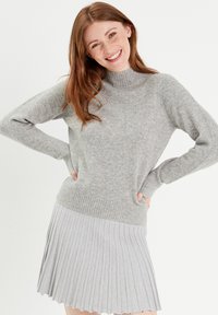 Pull en maille grise avec un col montant, des poignets côtelés et une jupe plissée gris clair. Le tissu est doux et texturé.