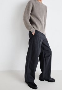 Grå ribstrikket sweater med rund hals, parret med løstsiddende sorte bukser og sorte ankelstøvler. Subtile teksturer og komplementære farver.