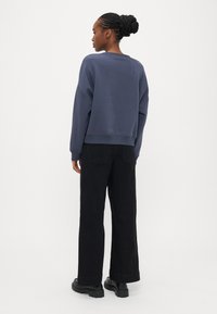 Felpa blu navy con una vestibilità comoda, collo rotondo e polsini a costine, abbinata a pantaloni neri a gamba larga e stivali neri chunky.