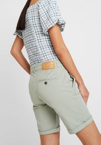 Světlé zelené bavlněné šortky s obráceným lemem, s kapsami na zadní straně a opáskou se světle hnědou koženou značkou v pase.