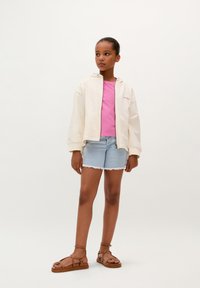 Lichtgekleurde crème zip-up hoodie, kort roze t-shirt, denim shorts met rafelige zoom, en bruine sandalen met bandjes. Eenvoudige, casual outfit.