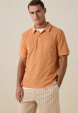 Oranje, gestructureerd poloshirt met een kraag, korte mouwen en een borstzak, gedragen over een wit onderhemd en gecombineerd met gestreepte broek.