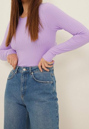 Haut long à manches ribbées violet clair associé à un jean en denim bleu taille haute, avec une fermeture à boutons et des poches avant.