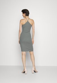 Vestido cinza, ajustado, feito de um tecido suave, com decote halter e detalhes discretos nas costas. Usado com sandálias de salto de cor clara.