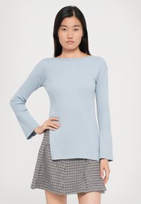 Light blue ribbed sweater with flared sleeves, paired with a plaid skirt. Sweater features a boat neckline and a slightly elongated hem.