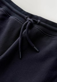 Tumesinised elastsed dressipüksid, millel on lai vöökoht, reguleeritav mustade otsikutega nöör ja sileda tekstuuriga kangas.