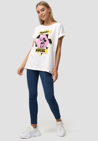 Witte t-shirt met korte mouwen met een roze en zwarte graphic van Mickey Mouse en de tekst "Mickey House". Gepaard met donkerblauwe skinny jeans.