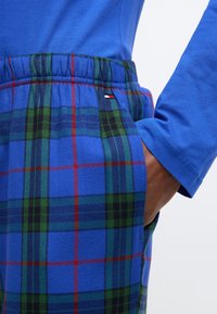 Modrý top s dlhým rukávom v kombinácii s károvanými nohavicami s modrou, zelenou a červenou farbou, elastickým pásom a bočným vreckom.