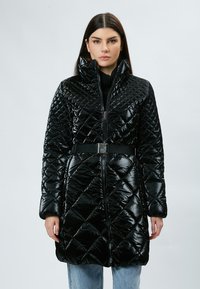 Abrigo acolchado negro con cuello alto, cierre de cremallera y cinturón desmontable. Acabado brillante y patrón de diamantes en toda su superficie.