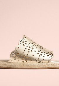 Guld lædersandal med cut-out blomsterdesign, bølget kant og vævet jute sål. Glat tekstur med en blank finish.