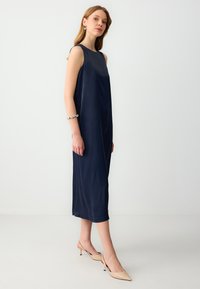 Navy ärmelloses Midikleid mit einem entspannten Schnitt, glatter Textur und seitlichen Schlitzen, kombiniert mit nudefarbenen spitzen High Heels.