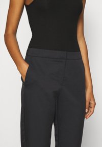 Svart rippad linne i kombination med mörkgrå skräddarsydda byxor som har en slät yta, rak passform och sidofickor.