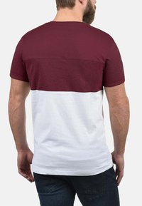 Maroons og hvid T-shirt med et tofarvet design, korte ærmer og en struktureret maroon øverste sektion. Glat hvid nederste sektion.