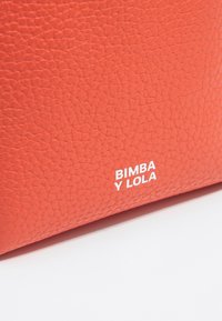 Oranžová textúrovaná kožená taška s jemnou zrnitou úpravou, s bielym potlačeným logom "BIMBA Y LOLA" na boku.