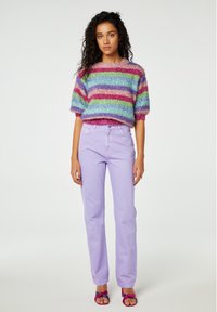 Multikleurige pluche trui met horizontale strepen in roze, blauw, groen en rood. Gekoppeld met lavendel rechte broek en roze sandalen.