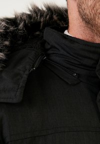 Fekete dzseki, műszőrme bélésű kapucnival, textúrált anyagból, cipzáros záródással és álló gallérral a melegségért.