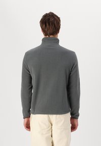 Pullover in pile grigio con colletto alto, maniche lunghe e una texture liscia. Il retro presenta cuciture minime e un design a vestibilità rilassata.