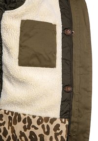 Intérieur d'une veste vert olive avec doublure en sherpa crème, petite poche en tissu, boutons marron et tissu à imprimé léopard au bord inférieur.