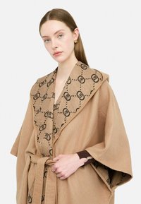 Avvolgente in misto lana di colore marrone con un colletto a contrasto a motivo, caratterizzato da disegni circolari neri. Legato in vita con una cintura coordinata.