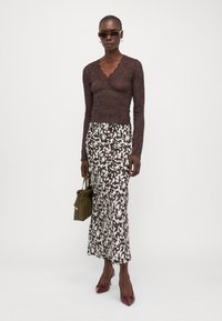 Brown lace long-sleeve top paired with a brown and white patterned maxi skirt. Accessories include a green bag and burgundy heels.