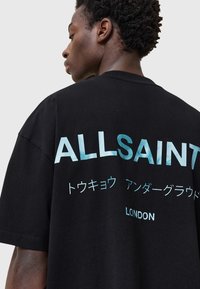Juodas medvilninis marškinėlis su dideliu tekstu "ALLSAINTS" mėlynos gradacijos spalva ant nugaros, papildomu tekstu japonų kalba ir "LONDON" žemiau.