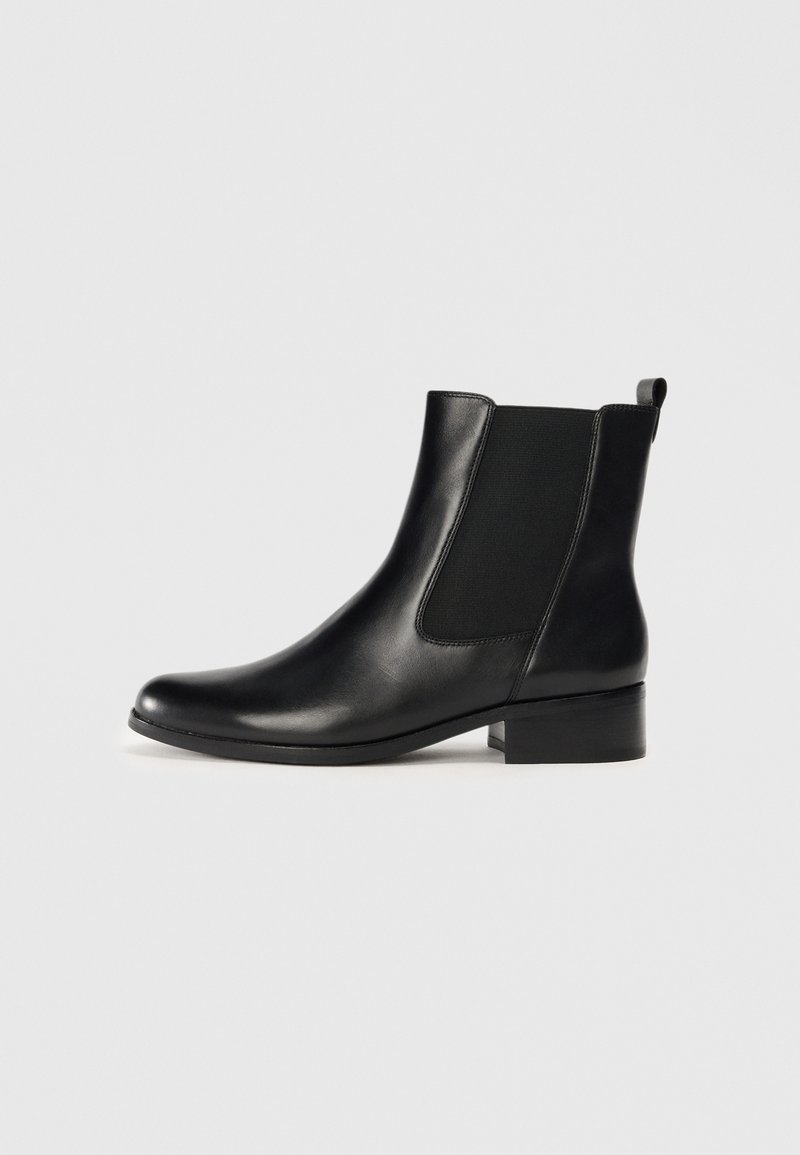 Botines de cuero negro con paneles laterales elásticos, puntera redondeada, tacón bajo y tira trasera para ponerlos fácilmente. Textura suave, diseño minimalista.