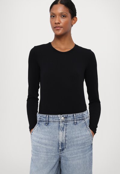Black long-sleeve top made of cotton, paired with light blue high-waisted denim jeans featuring a button closure and side pockets.