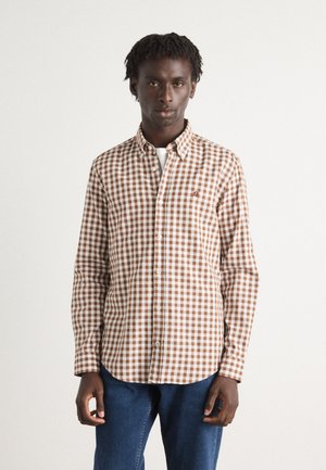 Camicia a quadri marrone e bianca con colletto, maniche lunghe e un piccolo logo sul petto; abbinata a jeans blu.