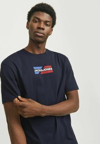 Marineblå kortærmet t-shirt lavet af bomuld, med et grafisk logo i blå og rød. Blød tekstur og afslappet pasform.