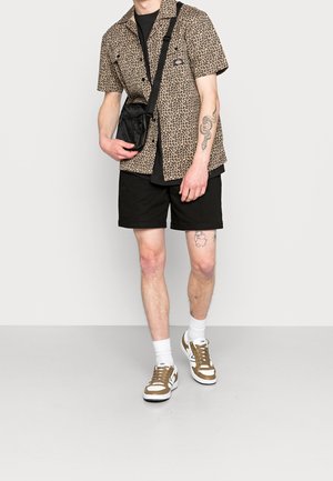 Korte mouwen blouse in luipaardprint, zwarte shorts en bruin/witte sneakers. Inclusief een zwarte schoudertas.