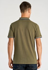 Olivgrünes Poloshirt mit kurzen Ärmeln, geripptem Kragen und marineblauem Besatz. Hergestellt aus einem strukturierten Baumwollmischgewebe mit geradem Schnitt.