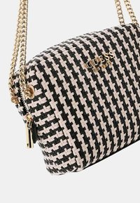 Borsa a tracolla intrecciata in nero e crema con dettagli in metallo dorato. Dotata di tracolla a catena e chiusura con zip per un facile accesso. Dettaglio del logo visibile.