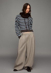 Pasekowany krótki sweter w ciemnobrązowym i jasnoniebieskim kolorze, zestawiony z szerokimi szarymi spodniami. Miękka tekstura, luźny krój, z kapturem.