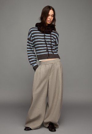 Sötétbarna és világoskék csíkos rövidített pulóver, széles szárú szürke nadrággal párosítva. Puha tapintású, laza fazonú, kapucnival díszítve.