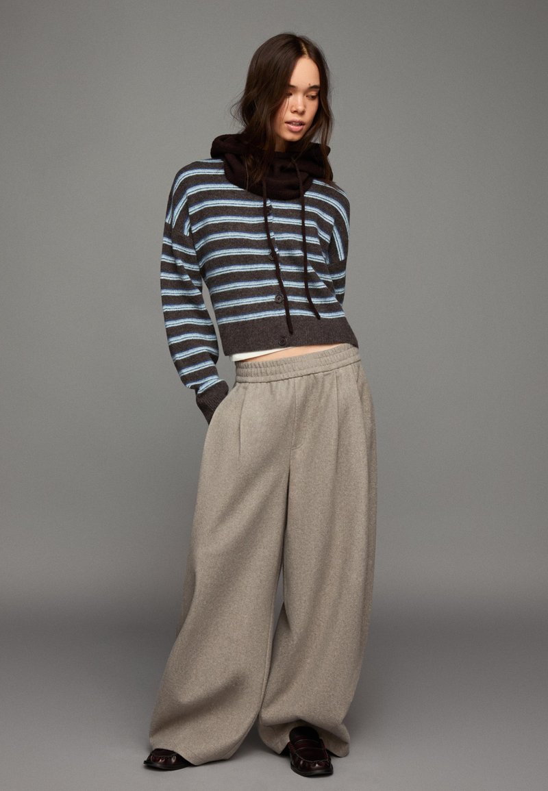 Pasekowany krótki sweter w ciemnobrązowym i jasnoniebieskim kolorze, zestawiony z szerokimi szarymi spodniami. Miękka tekstura, luźny krój, z kapturem.