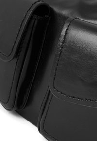 Sac en cuir noir avec deux poches avant à rabat, texture lisse et détails de surpiqûres contrastantes.