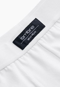 Ceinture blanche à texture froncée avec une étiquette en tissu noire. L'étiquette affiche "ombre" en lettres blanches et "VÊTEMENTS MESSIEURS" en dessous.