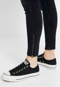 Černé plátěné tenisky s bílými gumu na špičkách, doplněné tmavě modrými skinny džíny se zipy na kotnících.